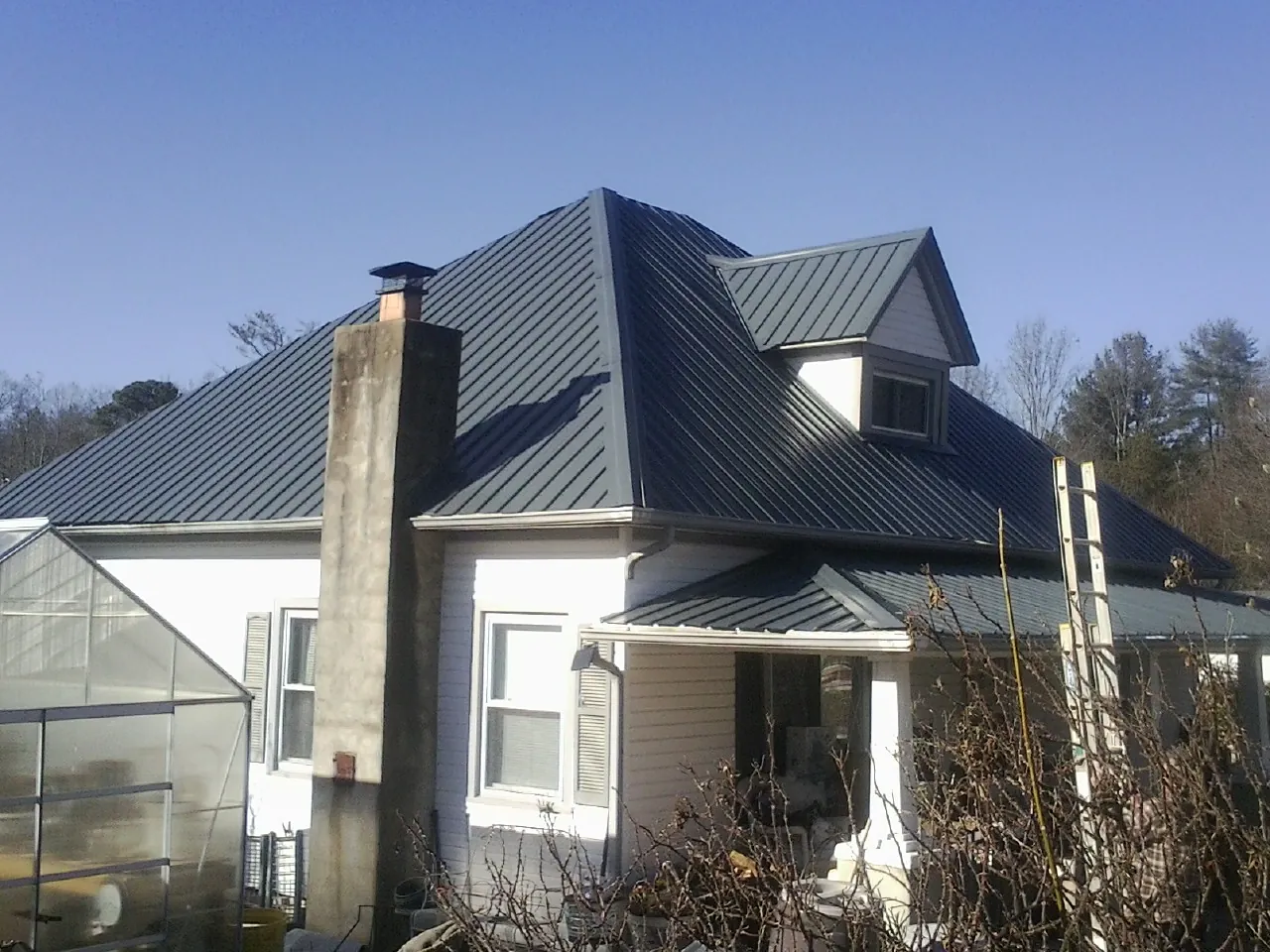 Dark blue standing seam metal roof on a white farmhouse with dormer — Slate & Tile Roof Repair by Roofing Brothers in Archbald