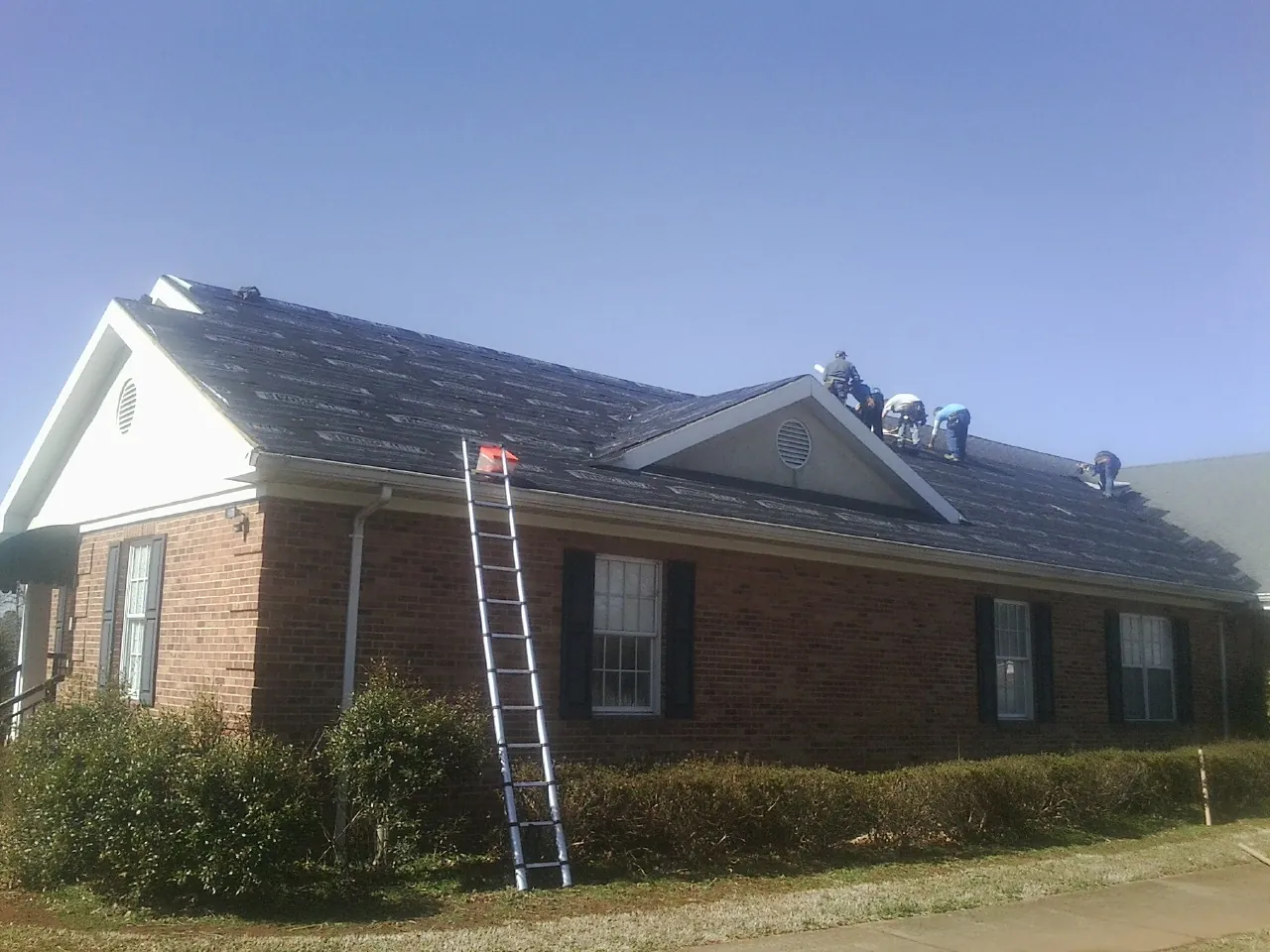 Crew tearing shingles off a brick ranch roof with a ladder set — Metal Roof Repair work by our crew in Archbald
