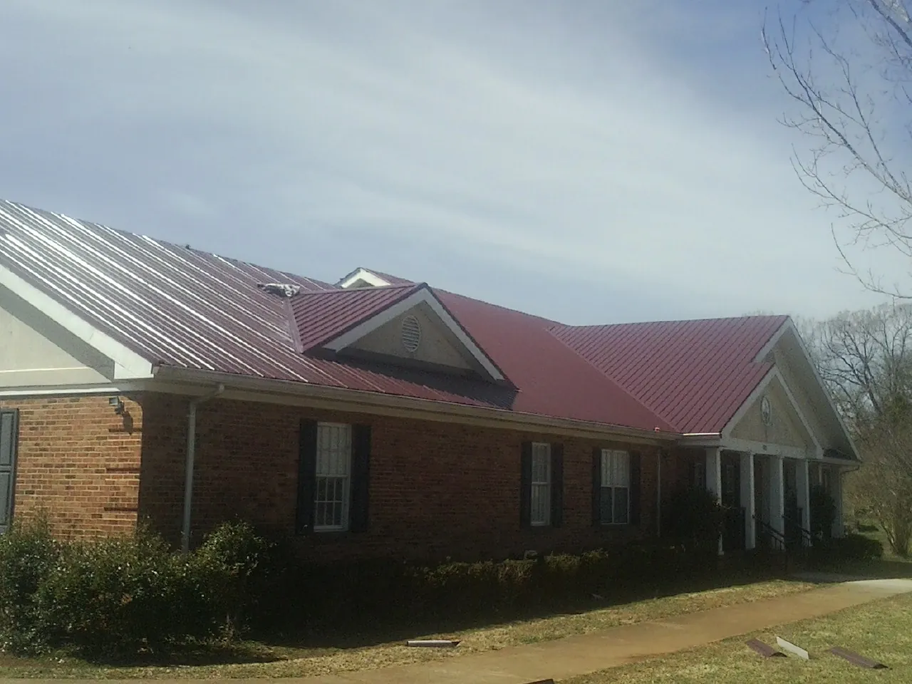 Red metal roof with gabled entries on a long brick building, from a Hail Damage Roof Repair job in Archbald