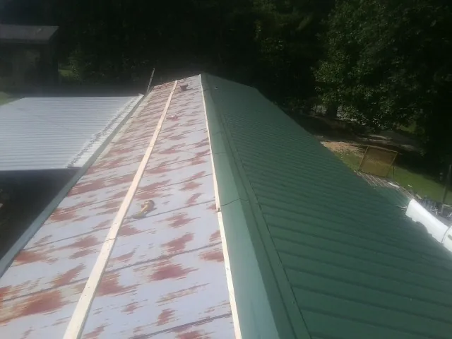Old rusted panels beside newly installed green metal roofing — Wind Damage Roof Repair by Roofing Brothers in Archbald