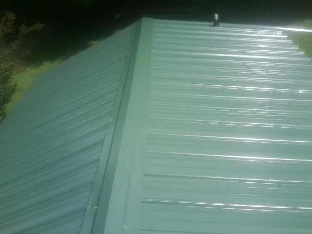 New green metal panels meeting at the ridge of a roof — Flat Roof Repair work by our crew in Archbald