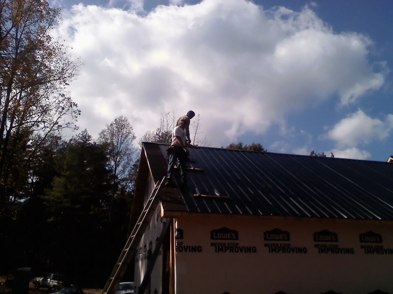 Roofer fastening dark metal panels high against a cloudy sky, from a Roof Inspection job in Archbald