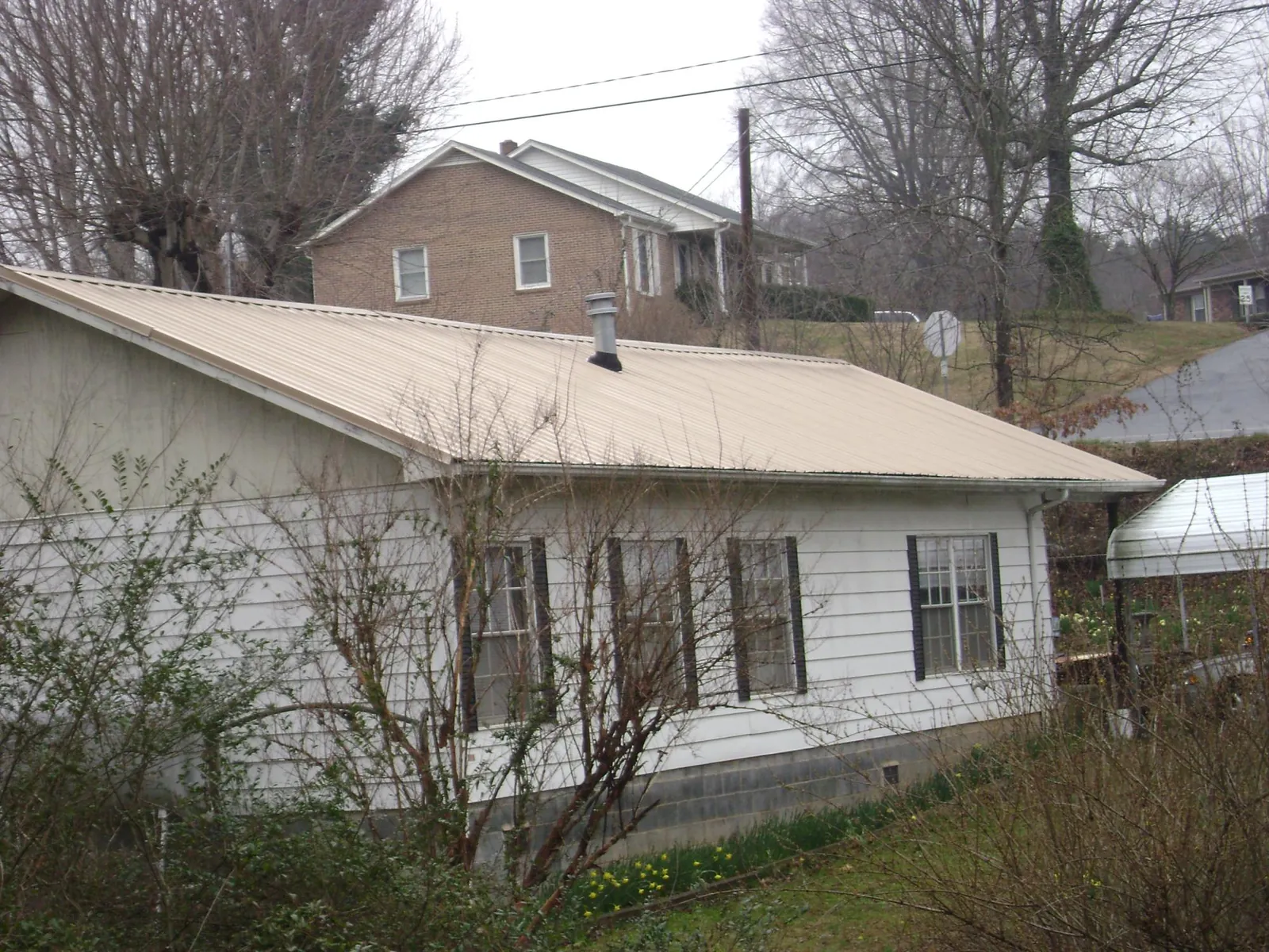 Tan metal roof on a white sided house set into a hillside — Commercial Roofing by Roofing Brothers in Archbald